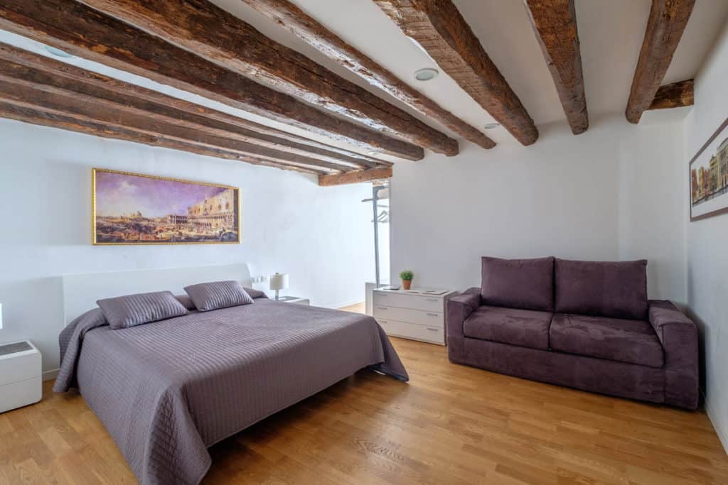 Right view of the luminous master bedroom with exposed beams and sofa - The Lion's 5 Apartment Right view of the luminous master bedroom with exposed beams and sofa - The Lion's 5 Apartment